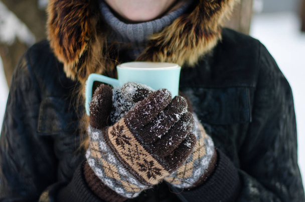 Gloved hands holding a cup of tea outdoors - Фото, изображение