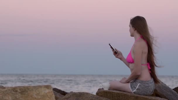 Menina em um maiô na praia sentado em uma rocha e disca inquieto o número de telefone
 - Filmagem, Vídeo