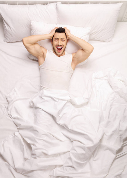 Frustrated guy lying in bed and screaming - Foto, imagen