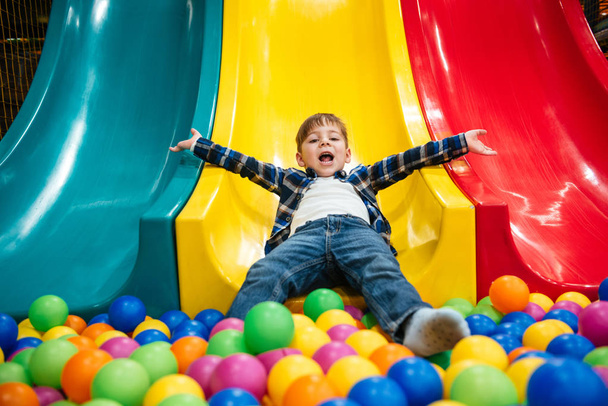 Little boy playing on slide and pool with colorful balls - Foto, imagen