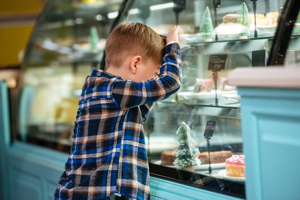 Little boy standing and leaning at shocase with cakes - Fotoğraf, Görsel