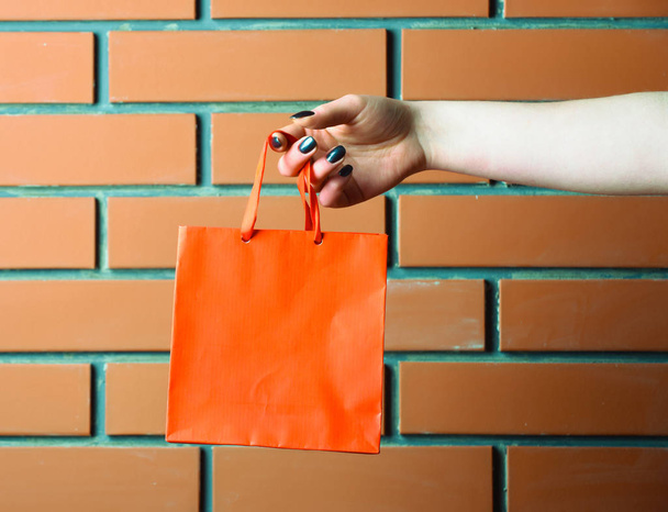 orange shopping bag in female hand on brick wall - Fotografie, Obrázek