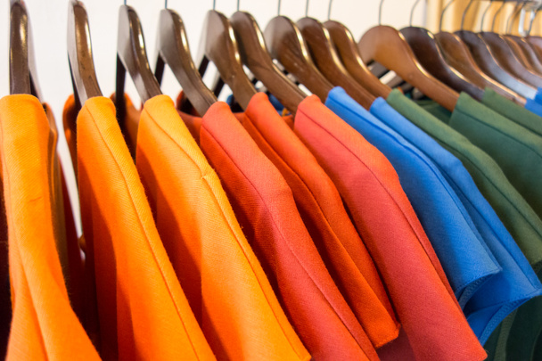 Line of multi colored clothes on wooden hangers in store. Sale - Photo, Image