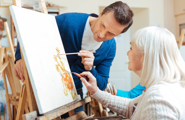 Serious artist helping elderly woman in painting school - Photo, image