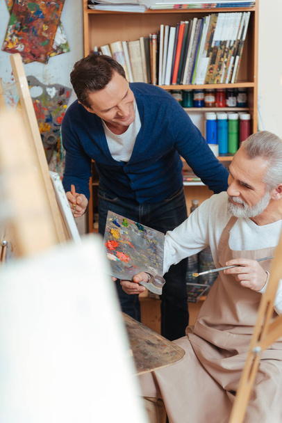 Lächelnder Künstler hilft älterem Mann beim Malen - Foto, Bild