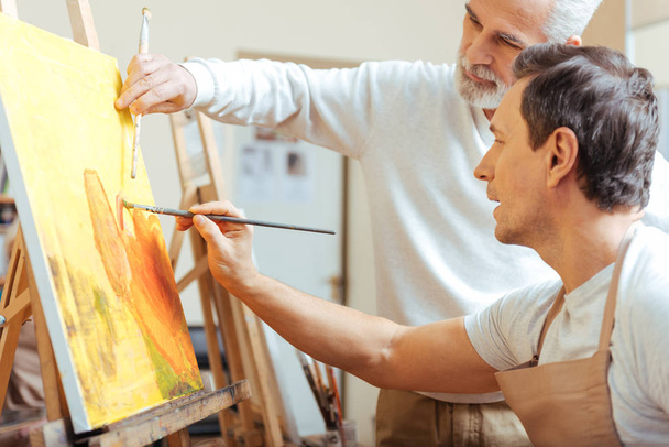 Elderly artist painting with his young colleague. - Photo, Image