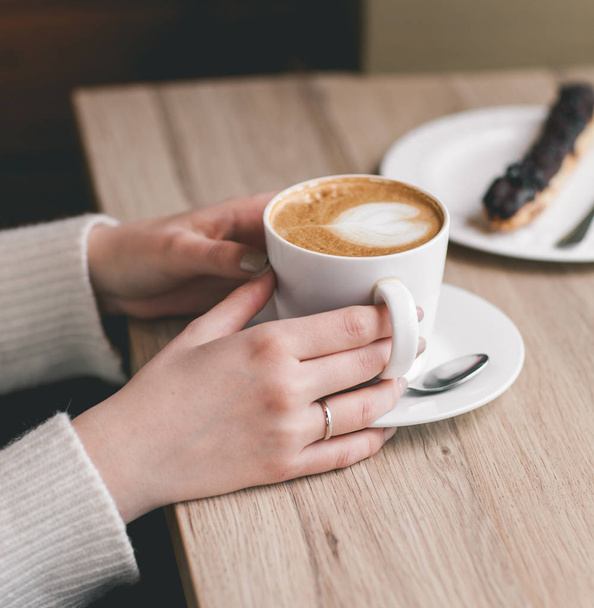 Womans hands wrapped around a cup on wood table with chocolate e - Photo, Image