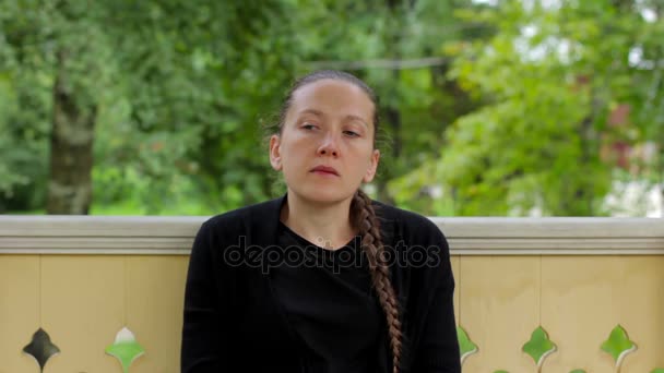 Portret van een peinzende meisje met vlecht gekleed in zwarte zitten in de gazebo - Video