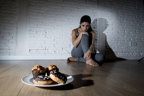 нездорові цукрові пончики і кекси і спокусила молоду жінку або дівчину-підлітка, що сидить на землі
 - Фото, зображення