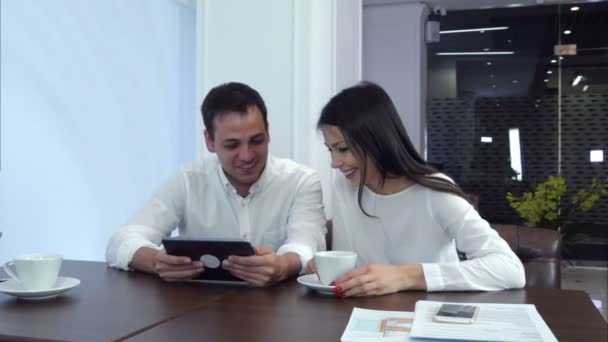 Mladý pár, směje se na něco zábavného na tabletu čekání na oběd - Záběry, video