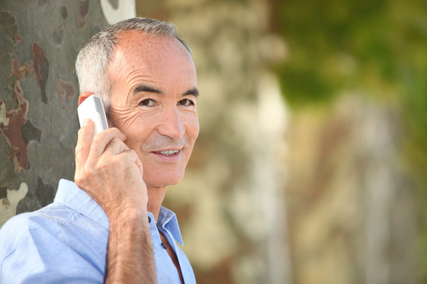 Grey haired man making telephone call in park - Foto, imagen