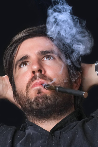 Young man smoking electronic cigarette on black background - Foto, Imagem