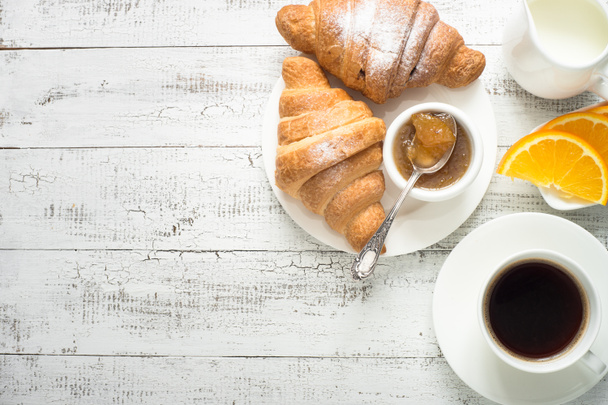 Croissant jam koffie oranje jice aan witte houten tafel.  - Foto, afbeelding