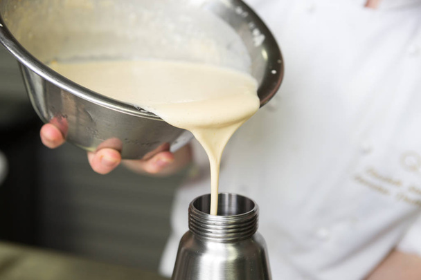 Thick fresh sweet dessert cream, being poured into a metal container in an industrial kitchen. - Foto, Imagem