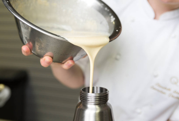 Thick fresh sweet dessert cream, being poured into a metal container in an industrial kitchen. - Fotoğraf, Görsel