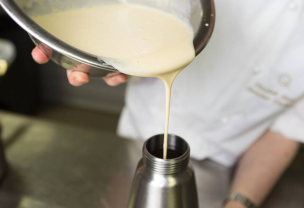 Thick fresh sweet dessert cream, being poured into a metal container in an industrial kitchen. - Foto, Bild