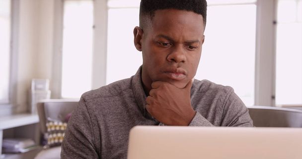 Молодой черный человек, работающий над ноутбуком из своего домашнего офиса
 - Фото, изображение