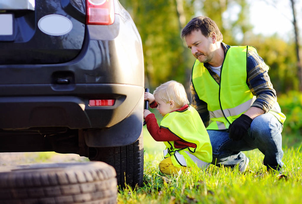Father and his little son repairing car and changing wheel together on summer day - Foto, imagen