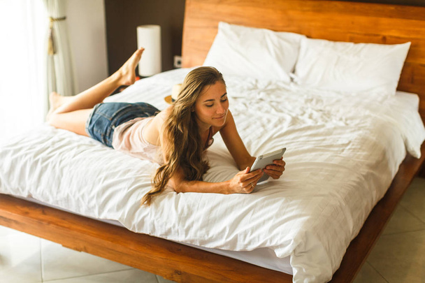 Young woman with tablet lying on the bed - Фото, изображение