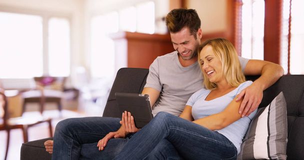 Sweet millennial couple sitting on couch and watching videos on tablet - Photo, Image