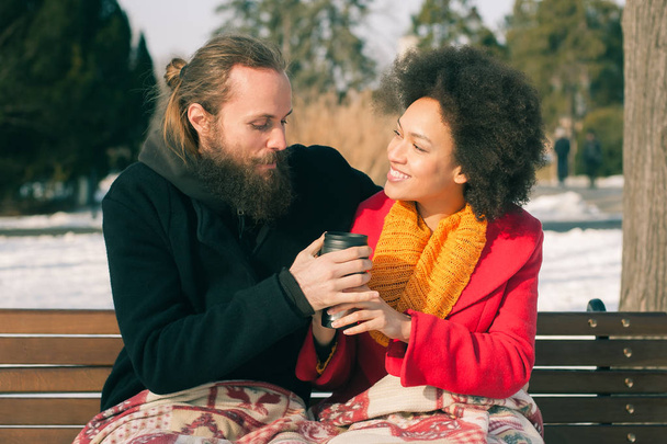 Loving couple with hot drinks sitting on bench in winter - Photo, Image