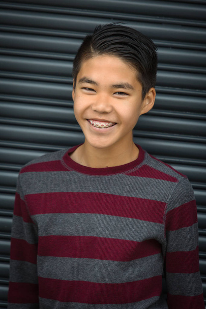 Teen asian boy with braces smiling set against dark background - Photo, Image