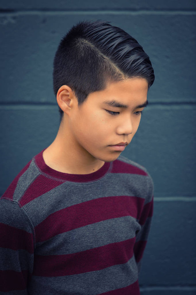 Triste adolescente asiático chico mirando hacia abajo, brazos sostenidos detrás de su espalda
. - Foto, imagen