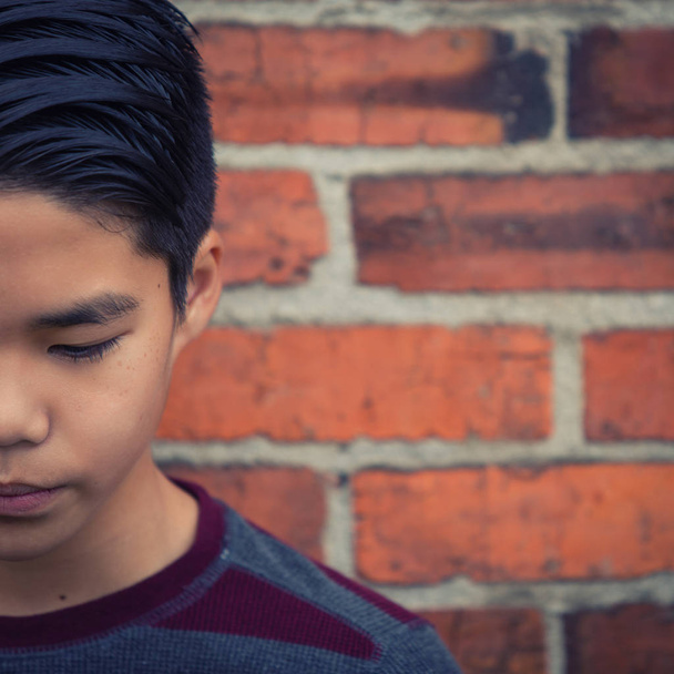 Artystyczny portret smutny nastoletni chłopiec azjatyckich, patrząc w dół. Celowo przycięte połowę twarzy efekt i stworzyć przestrzeń otwarta dla tekstu. - Zdjęcie, obraz