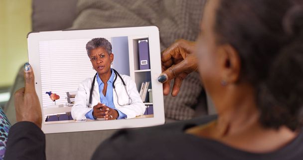 Μια ηλικιωμένη μαύρη γυναίκα μιλώντας με το γιατρό της αφρικανικής αμερικανικής μέσω βίντεο chat - Φωτογραφία, εικόνα