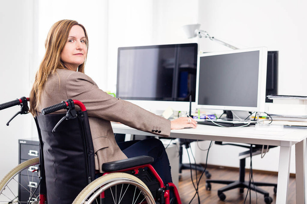 Woman Sitting In Wheelchair Working In Modern Office - 写真・画像