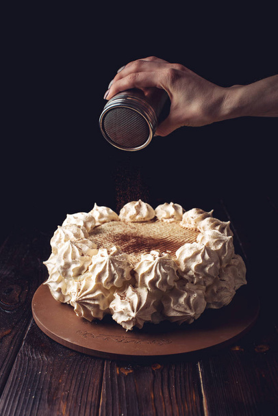 Рука посипає какао на красивому білому торті
 - Фото, зображення