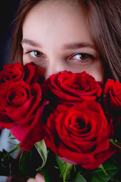 Pretty girl is holding a bouquet of red roses, dark background - Φωτογραφία, εικόνα