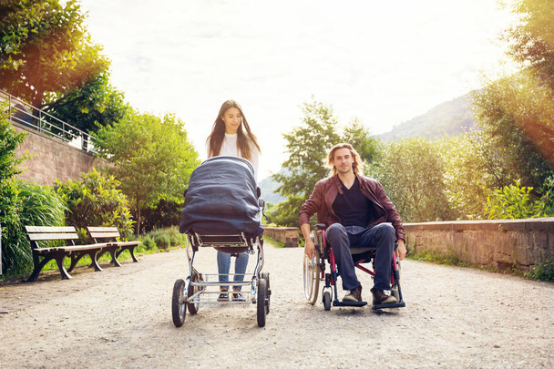 Young Parents In Wheelchair With Baby Stroller In The Park - Φωτογραφία, εικόνα