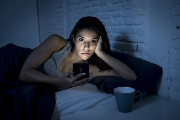 jeune belle femme latine sur le lit tard dans la nuit textos en utilisant le téléphone mobile somnolent et fatigué
 - Photo, image