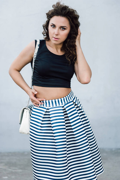 Beautiful sexy young brunette girl with long wavy hair thin slender figure and pretty face make-up wearing a long stripped skirt and black top, high heels. Walk on the street in casual style - Fotoğraf, Görsel