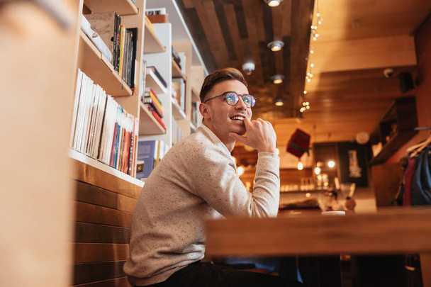 Smiling man wearing glasses sitting in cafe - Фото, изображение