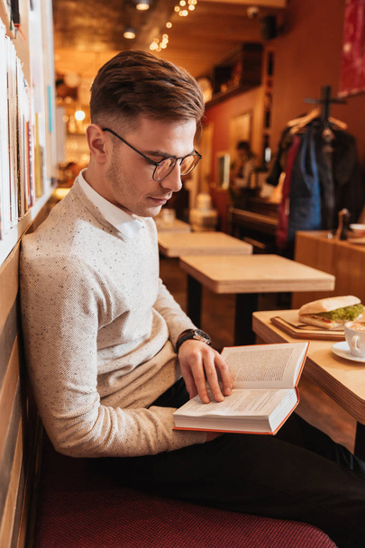 Young handsome man sitting in cafe while reading book. - Foto, Imagem