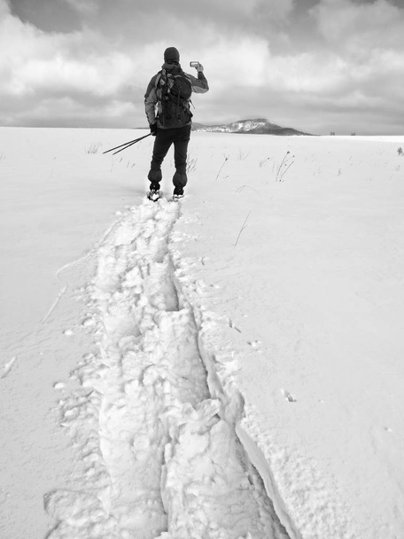 スノー シューズとバックパックのスマート フォンで写真を撮る男。雪の吹きだまりでハイカー - 写真・画像