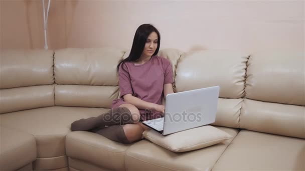 Young Brunette Girl In a Warm Socks Stockings, Lays On Leather Sofa at Home And Working On Laptop - Filmati, video