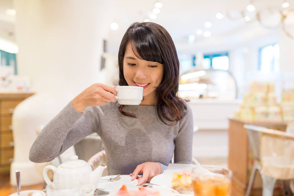 Vrouw geniet van haar koffie bij cake shop - Foto, afbeelding