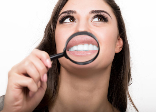 portrait of young woman showing teeth and tongue through magnifying glass - Photo, image