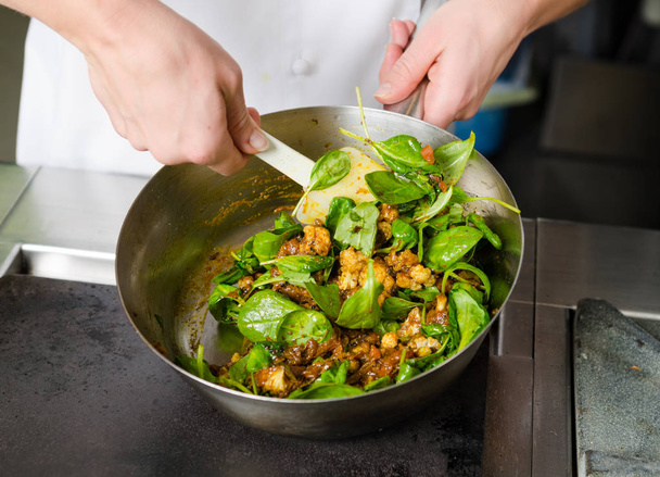 Mixing a curried cauliflower, spinach and potato sauce, in a metal pan. - Foto, afbeelding
