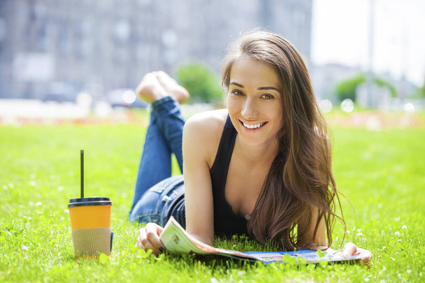 Young woman reading magazine lying on grass - Zdjęcie, obraz