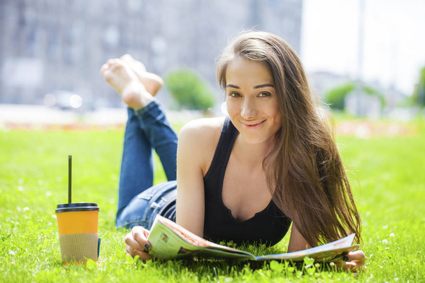 Young woman reading magazine lying on grass - Valokuva, kuva