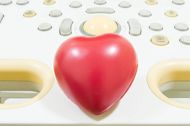 Figura corazón se encuentra en el mando a distancia o teclado de la máquina de ultrasonido. Fotografía conceptual para el diagnóstico de cardiodiagnósticos o afecciones cardíacas por ultrasonido en niños y adultos
 - Foto, Imagen