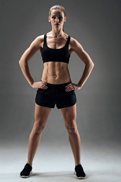 Athletic girl demonstrating her muscles on a grey background - Foto, Imagen