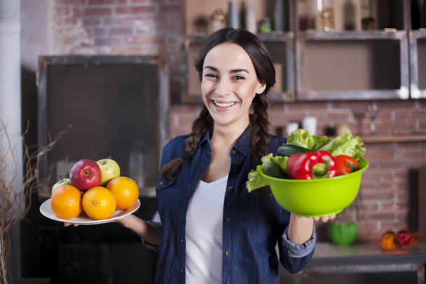Young Woman in the kitchen. Healthy Food. Dieting Concept. Healthy Lifestyle. Cooking At Home. Prepare Food. Very Beautiful cheerful young brunette woman holding fruits and vegetables and smiling. - Foto, immagini