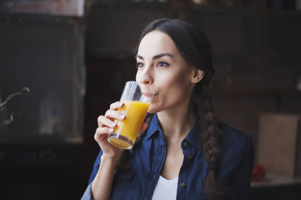 Portret van zeer mooie jonge brunette meisje in jeans overhemd op een keuken thuis. Meisje lachen en jus d'orange te houden in een transparant glas. - Foto, afbeelding
