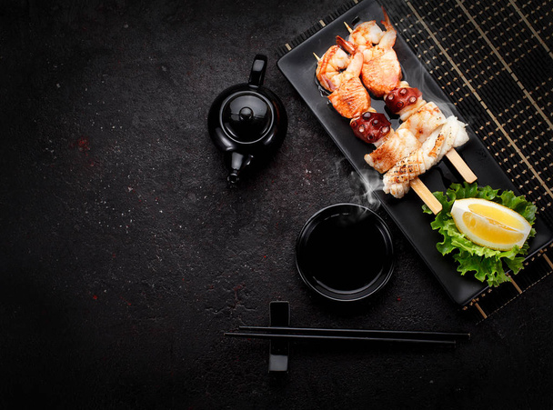Tasty seafood skewers and soy sauce over dark concrete background - Foto, immagini