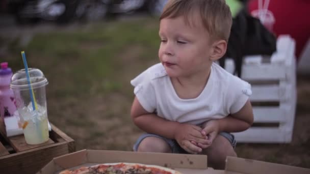 Young beautiful woman and little boy have a rest at park in summer day. Boy eating pizza and then points to his mother. - Filmati, video